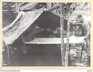 SOUTH BOUGAINVILLE. 1945-07-21. PRIVATE S. ROBERTSON (1), AND PRIVATE L.M. DENNIS (2), MEMBERS OF THE 58/59 INFANTRY BATTALION, SHIFTING THEIR BUNKS WHEN THEIR TWO-MAN TENT BECAME FLOODED. THE ..