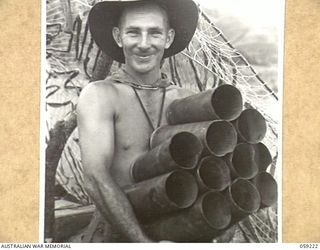 KUMBARUM, NEW GUINEA, 1943-10-23. VX16121 SERGEANT F.E. GRAY OF THE 54TH BATTERY, 2/4TH AUSTRALIAN FIELD REGIMENT CARRYING A LOAD OF EMPTY 25-POUNDER CHARGE GUN CASES