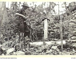 YAULA, NEW GUINEA. 1944-04-10. VX93433 CAPTAIN W. A. DARGIE, OFFICIAL WAR ARTIST, MILITARY HISTORY SECTION, EXAMINES THE WORK OF A JAPANESE CRAFTSMAN WHO BUILT THIS SMALL SHRINE ALONGSIDE THE ROAD ..