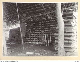 ULEBILUM RIDGE, YAMIL SECTOR, NEW GUINEA, 1945-07-08. STAFF-SERGEANT A.F.S. JONES, 2/5 SUPPLY DEPOT COMPANY (1), STACKING MORTARS BROUGHT IN BY NATIVE CARRIERS FROM THE DROPPING ZONE. MORE THAN 110 ..