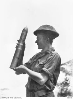 PAPUA, NEW GUINEA. 1942-10. CORPORAL NORM ROSE, 2/33 BATTALION, HOLDING A 75 MILLIMETRE JAPANESE SHELL FOUND IN A GUN POSITION ON IORIBAIWA RIDGE