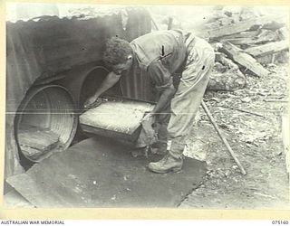 HANSA BAY-SEPIK RIVER AREA, NEW GUINEA. 1944-08-03. QX50240 CORPORAL R.N.W. THOMAS COOK, 5TH DIVISION SALVAGE UNIT REMOVING A TRAY OF BUNS FROM THE OVEN