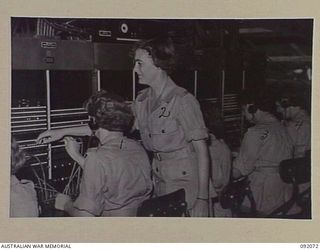 LAE, NEW GUINEA, 1945-05-20. SGT M. JONES (2), MONITORING THE BOARD OF THE NEW SWITCHBOARD AT SIGNALS, HQ FIRST ARMY. THE HUT IS NOT YET COMPLETE AND THE GIRLS ARE WORKING IN A MAZE OF BEAMS AND ..