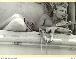 AT SEA. 1945-03-26. PRIVATE C. COOPER, A COMPANY, 2/48 INFANTRY BATTALION, LETTER WRITING WHILE PERCHED IN THE SUPERSTRUCTURE OF THE VAN HEUTSZ DURING THE EMBARKATION OF HEADQUARTERS 26 INFANTRY ..