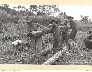 EVAPIA RIVER, NEW GUINEA, 1944-03-15. MEMBERS OF THE 2/4TH FIELD COMPANY, ROYAL AUSTRALIAN ENGINEERS, POSITIONING WOODEN ROLLERS SO AS TO LIFT THE HUGE MAIN SUPPORT FOR THE SUSPENSION BRIDGE UNDER ..