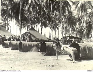 MILILAT, NEW GUINEA. 1944-09-03. NX193454 PRIVATE J.K. GREBERT STRUGGLING THROUGH THE BARRELS DURING THE OBSTACLE RACE AT THE SPORTS MEETING ORGANISED BY HEADQUARTERS, 5TH DIVISION TO COMMEMORATE ..