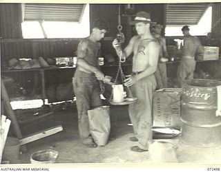 PORT MORESBY, NEW GUINEA. 1944-04-21. NX112901 PRIVATE M. COLLINS (1), WITH NX113666 PRIVATE L. HUDSON (2), AT A DETAILS ISSUE DEPOT, AUSTRALIAN ARMY SERVICE CORPS WEIGHING PEAS FOR DISTRIBUTION TO ..
