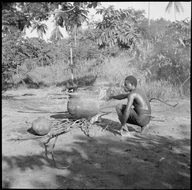 Aiau, the Chinnery's garden boy, squatting by a cooking pot, Malaguna Road, Rabaul, New Guinea, ca. 1936 / Sarah Chinnery