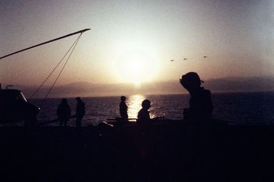 Flight deck crewmen aboard the amphibious assault ship USS GUAM (LPH 9) are silhouetted in the early morning sun during operations off the coast of Beirut, Lebanon