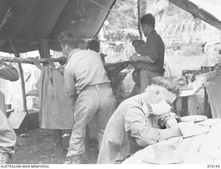 KOROPA, NEW GUINEA. 1944-02-03. QX6083 MAJOR J.J. RYAN, MC (1), A SURGEON OF THE 2/1ST GENERAL HOSPITAL ATTACHED TO THE 15TH FIELD AMBULANCE, STILL WEARING A SURGICAL MASK, WRITES THE HISTORY OF AN ..