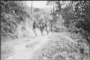 Group of people walking along a road carrying trunks and packages, New Guinea, ca. 1929 / Sarah Chinnery