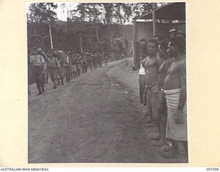 WEWAK AREA, NEW GUINEA. 1945-09-21. NATIVES LINING THE ROAD AS SOLDIERS OF 18 JAPANESE ARMY PASS ALONG THE ROAD ON THEIR WAY TO THE CONCENTRATION AREA ON MUSCHU ISLAND. THE JAPANESE HAVE BEEN ..