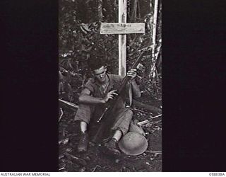 FARIA VALLEY, NEW GUINEA, 1943-10-20. SX30661 PRIVATE J. G. HOFFMAN OF THE 2/27TH AUSTRALIAN INFANTRY BATTALION, CLEANING HIS RIFLE BESIDE A GRAVE IN THE JUNGLE AT GUY'S POST