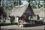 People on the veranda of Momwaroka's house, pig underneath