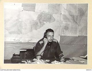 CAPE CUNNINGHAM, NEW BRITAIN, 1945-08-15. MAJOR C.D. BATES, DISTRICT OFFICER, HEADQUARTERS AUSTRALIAN NEW GUINEA ADMINISTRATIVE UNIT, RABAUL DISTRICT, MAKING ARRANGEMENTS ON THE PHONE FOR EXTRA ..