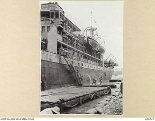 MILNE BAY, NEW GUINEA. 1942-09-14. A SHIP UNLOADING MEN AND EQUIPMENT AT PONTOON WHARF. IN THE CASE OF HEAVY LIFTS, MOTOR TRANSPORT IS ABLE TO BACK DOWN PLANKS TO PONTOON AT SHIP'S SIDE