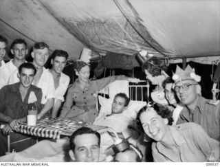 RABAUL, NEW BRITAIN, 1945-12-22. PATIENTS AND STAFF IN WARD 4, (EAR, NOSE AND THROAT), GATHERED AROUND CORPORAL R. MCKAY WHO WAS TOO ILL TO GET OUT OF BED, TO CHEER HIM DURING THE CHRISTMAS PARTY ..