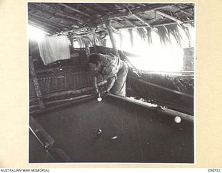 KARAWOP, NEW GUINEA, 1945-09-18. TPR W.G. TYLER, 2/6 CAVALRY COMMANDO REGIMENT CAREFULLY PLAYING A SHOT ON THE UNIT'S BILLIARD TABLE WHICH IS ALWAYS IN GREAT DEMAND