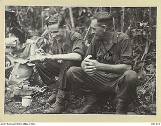 BOUGAINVILLE. 1945-04-30. PRIVATE A.E. CONNELL (1), AND PRIVATE F.D. JONES (2), MEMBERS OF 9 INFANTRY BATTALION, ENJOYING A HOT MEAL ON THE HATAI TRACK AFTER A LONG WALK FROM ANDERSON'S JUNCTION TO ..