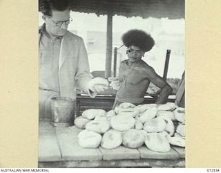 MILNE BAY, NEW GUINEA. 1944-04-20. THE HONOURABLE E.J. WARD, MINISTER FOR EXTERNAL TERRITORIES IN THE AUSTRALIAN GOVERNMENT, EXAMINING BREAD MADE FROM WHOLEMEAL AND OTHER INGREDIENTS IN THE BAKE ..