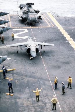 A plane director signals to the pilot of an AV-8B Harrier aircraft taxiing on the flight deck of the amphibious assault ship USS SAIPAN (LHA-2) during a rehearsal for Operation Sharp Edge. The SAIPAN is on station off the coast of Liberia