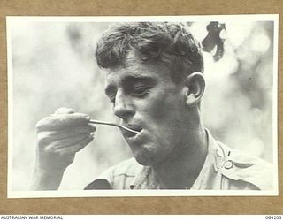 GEYTON'S POST, NEW GUINEA. 1944-01-19/20. QX11753 PRIVATE J.E.C. WADE OF THE 2/5TH FIELD AMBULANCE ENJOYING LUNCH AT THE NEW UNIT DRESSING STATION AT GEYTON'S POST