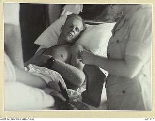 TOROKINA, BOUGAINVILLE. 1945-04-19. CORPORAL N.E. KRETSCHMANN (1), A PATIENT AT 2/1 GENERAL HOSPITAL WHO IS UNABLE TO WALK TO THE RECREATION HUT, HAS MATERIAL BROUGHT TO HIM BY RED CROSS MEMBERS