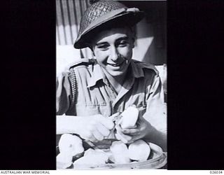 PAPUA NEW GUINEA. 1942-07. THIS IS CARMEN MIRANDA, STAR OF THE PORT MORESBY CONCERT PARTY, BACK TO EARTH AND ON THE JOB GETTING SOME "SPUDS" READY FOR AN UNTHEATRICALLY-MINDED COOK. PRIVATE MAURICE ..