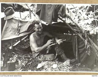 FINSCHHAFEN, NEW GUINEA. 1943-10-30. SX13243 PRIVATE S. A. HOARE OF STRATHALBYN, SA, AND OF HEADQUARTERS, 26TH AUSTRALIAN INFANTRY BRIGADE CLEANING HIS OWEN GUN IN FRONT OF HIS SLEEPING QUARTERS