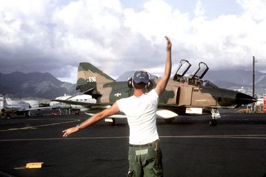 A ground crewman directs an RF-4C Phantom II aircraft into a parking spot while on a rest stop during Operation Coronet Hook, the redeployment of 22 F-4 and RF-4C Phantom II aircraft from Udorn Royal Thai Air Force Base, Thailand, and Kadena Air Base, Okinawa, to the United States because of a reduction in forces