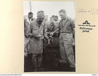 WEWAK AREA, NEW GUINEA, 1945-05-23. PTE C.M. TRELOAR (1), AT THE HQ COMPANY COOKHOUSE, 2/8 INFANTRY BATTALION, SERVING TEA TO ONE OF THE INDIANS WHO ESCAPED FROM THE JAPANESE