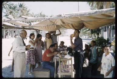 Ned Glass Marsters and unidentified men and children, at First Family umukai table during Empire Day celebrations, Palmerston Island