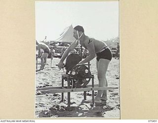 LAE, NEW GUINEA. 1944-08-27. CORPORAL K R W MILLER, REELMAN, OPERATING ONE OF THE REELS DURING THE REST AND RECREATION SURF RESCUE EVENT AT THE SURF CARNIVAL ORGANISED BY HEADQUARTERS, 5TH DIVISION ..