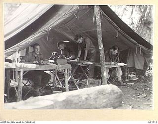 WEWAK AREA, NEW GUINEA, 1945-06-28. INTELLIGENCE SECTION AT WORK AT BATTALION HEADQUARTERS, 2/8 INFANTRY BATTALION. PRIVATE R. WINTER (2) AND SERGEANT L.M. PORTER (3) ARE STUDYING AERIAL ..