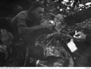 QX62698 Private Hector Gordon Alexander MacDonald, a 42nd Battalion medical orderly (left) giving a drink of water to Q272652 Private Kenneth George Merritt, also 42nd Battalion, who was wounded ..