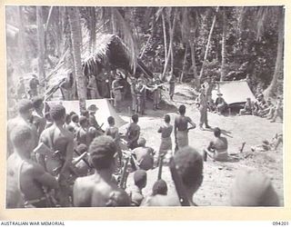 OINYALIB, NEW GUINEA. 1945-07-15. NATIVES OF 2 NEW GUINEA INFANTRY BATTALION WATCHING VX104911 CORPORAL JAMES RICHARD. WHITBOURNE (1), ENTERTAINING WITH SOME CLEVER JUGGLING DURING A CONCERT ..