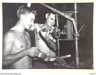 JACQUINOT BAY, NEW BRITAIN, 1945-08-31. PRIVATE L.V. BALL (1) AND CRAFTSMAN K.G. DAVEY (2) MEMBERS OF 141 HEAVY ANTI-AIRCRAFT BATTERY ROYAL AUSTRALIAN ARTILLERY USING A DRILL IN THE WORKSHOP
