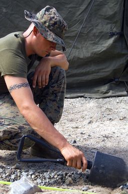US Marine Corps (USMC) Private First Class (PFC) Overturf, Eco Company, 2nd Battalion, 3rd Marine Regiment (2/3), Marine Corps Base Hawaii (MCBH), Hawaii (HI), uses an E-Tool (USMC Improved Entrenching Tool) to create the outer border of a terrain model at CROCODILE 2003