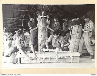 NADZAB, NEW GUINEA. 1944-05-25. MEMBERS OF THE 3RD AIR MAINTENANCE COMPANY ASSEMBLING PACKS FOR A PARACHUTE DROP TO TROOPS IN FORWARD AREA. IN THE FOREGROUND A SUPPLY PACK FOR A CONSOLIDATED ..