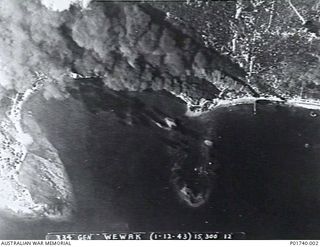 Wewak, New Guinea. 1943-12-01. Aerial photograph of thick black smoke billowing up from the harbour foreshore, possibly after attack by aircraft of the United States Army Air Force