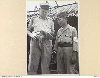 MUSCHU ISLAND, NEW GUINEA. 1945-10-27. CAPTAIN A.G. HICKS, 6 DIVISION PROVOST COMPANY, AND A JAPANESE OFFICER INSPECTING A PAIR OF BOOTS, PART OF A SHIPMENT OF JAPANESE EQUIPMENT FROM THE FORMER ..