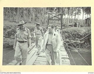 MILNE BAY, NEW GUINEA. 1944-04-20. THE HONOURABLE E.J. WARD, MINISTER FOR EXTERNAL TERRITORIES IN THE AUSTRALIAN GOVERNMENT (3), WITH MEMBERS OF HIS OFFICIAL PARTY CROSSING A SUSPENSION BRIDGE TO ..