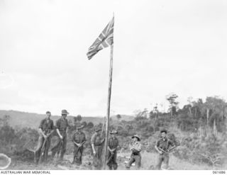 WAREO, NEW GUINEA. 1943-12-09. GROUP OF OFFICERS AND MEN OF THE 2/23RD AUSTRALIAN INFANTRY BATTALION, GROUPED AROUND THE UNIT VICTORY FLAG. THIS FLAG WAS PREVIOUSLY RAISED OVER KOKODA, BUNA AND ..