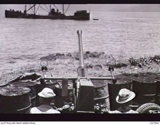 LAE, NEW GUINEA. 1943-10-04. TWO GUNNERS AND A BOFORS GUN OF "D" BATTERY, 102ND COAST ARTILLERY BATTALION, ANTI AIRCRAFT, UNITED STATES ARMY, WITH CAMOUFLAGE REMOVED. NOTE THE SMALL FREIGHTER IN ..