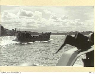 SIAR, NEW GUINEA. 1944-07-25. SILHOUETTED AGAINST THE SUN, BARGES CARRYING TROOPS OF THE 7TH INFANTRY BRIGADE FROM MADANG, MOVE INTO THE BAY