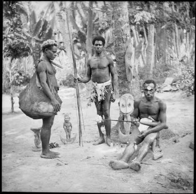 Seated man with a lime gourd and two standing men, one holding spears and one with a bilum, New Guinea, ca. 1936 / Sarah Chinnery