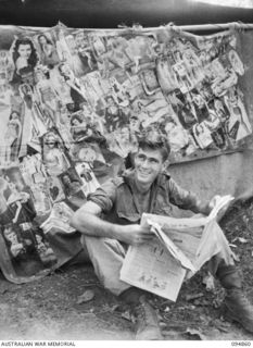 YAMIL 2, NEW GUINEA, 1945-08-01. PTE H. TEMPEST, 2/6 INFANTRY BATTALION, PHOTOGRAPHED WITH ALL HIS PIN- UP GIRLS WHICH HE HAS PASTED TO THE OUTSIDE OF HIS GROUND SHEET