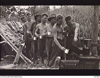 KAIAPIT, NEW GUINEA. 1943-09-24. TROOPS OF THE 7TH AUSTRALIAN DIVISION STATION COMMAND AT THE AIRSTRIP, LINE UP FOR A CUP OF TEA AT THE OUTDOOR COOKHOUSE