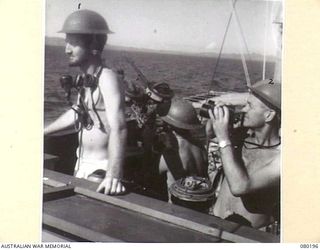 SUB-LIEUTENANT D.R. ROSS (1), GUNNERY OFFICER, ROYAL AUSTRALIAN NAVAL RESERVE, DIRECTING FIRE FROM THE BRIDGE WHILE LIEUTENANT R.C. POCKLEY, CAPTAIN, ROYAL AUSTRALIAN NAVAL VOLUNTEER RESERVE (2), ..