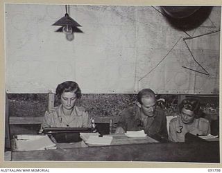 LAE, NEW GUINEA. 1945-05-15. SERGEANT M.J. SPENCER (1), AND CORPORAL V. GRAHAM (3), AT THE CAMP COMMANDANT'S OFFICE HEADQUARTERS FIRST ARMY, RECEIVING INSTRUCTION FROM SERGEANT E.J. GILROY (2), IN ..